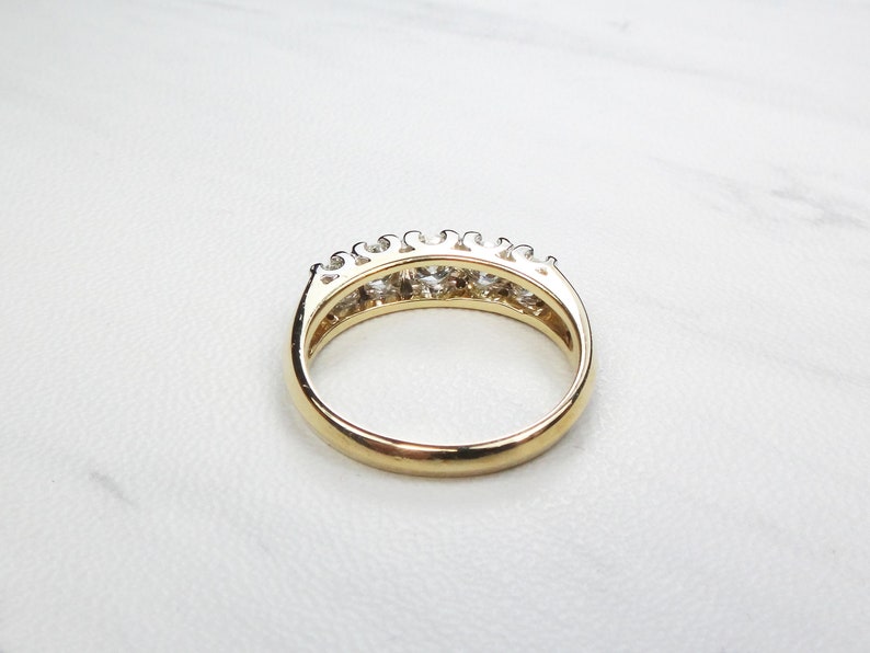 May include: A gold band ring with a row of clear round gemstones set in a prong setting.