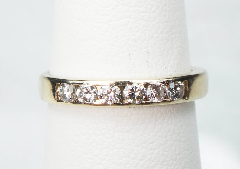 May include: A gold band with a row of small, clear diamonds set in the metal.
