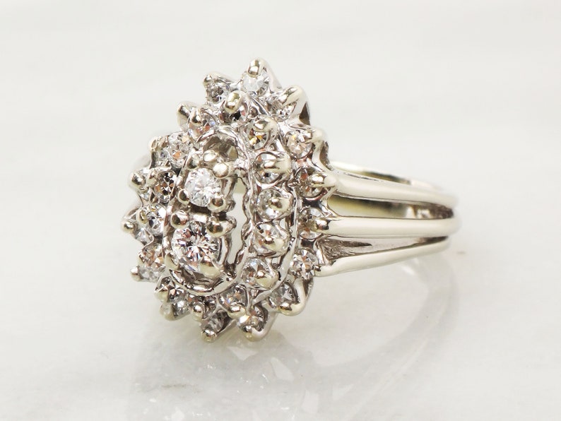 Op de afbeelding: Een zilveren ring met een traanvormige cluster van diamanten. De ring heeft een drievoudig bandontwerp.