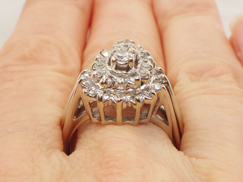 Op de afbeelding: Een zilveren ring met een grote, meerlaagse diamantcluster. De ring is bezet met veel kleine diamanten, waardoor een sprankelend effect ontstaat.