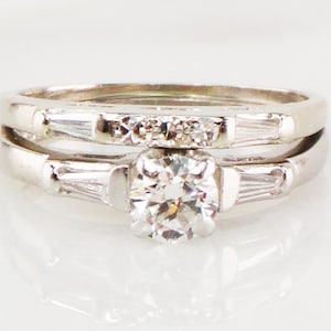 May include: A set of two silver engagement rings with a round center diamond and baguette diamonds on the band.