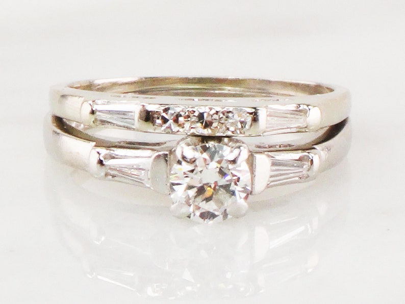 May include: A set of two silver engagement rings with a round center diamond and baguette diamonds on the band.