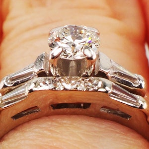 May include: A platinum engagement ring set with a large round brilliant diamond and a band of smaller diamonds. The ring is set with baguette diamonds on the sides.