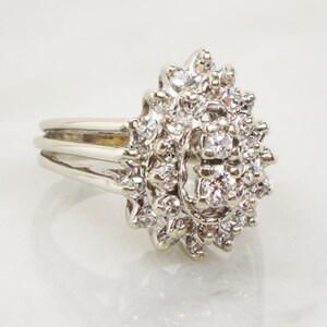 Op de afbeelding: Een zilveren ring met een grote cluster diamanten gezet in een bloemmotief.