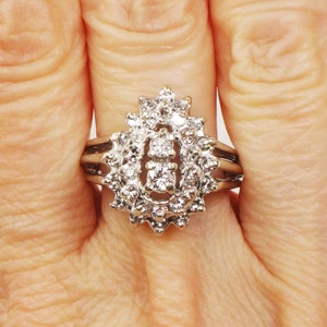 Op de afbeelding: Een zilveren ring met een grote ovale cluster van kleine diamanten. De ring heeft een delicate band met drie rijen kleinere diamanten.