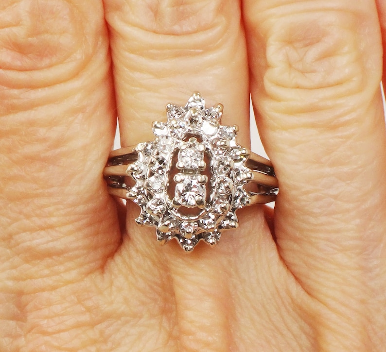 Op de afbeelding: Een zilveren ring met een grote ovale cluster van kleine diamanten. De ring heeft een delicate band met drie rijen kleinere diamanten.