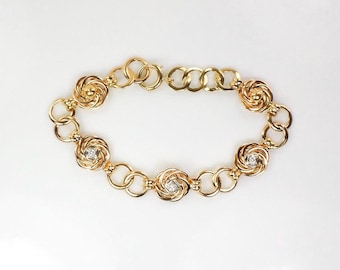 May include: A gold chain bracelet with five decorative rose-shaped links, each with a small clear stone in the center.