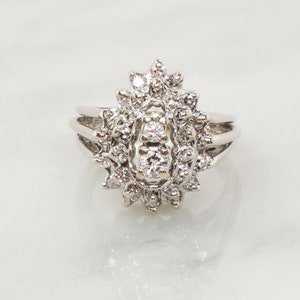 Op de afbeelding: Een zilveren ring met een grote, ovale cluster van diamanten. De ring heeft een delicate band en een middelste steen die omringd is door kleinere diamanten.