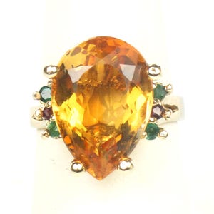 May include: A gold ring with a large pear-shaped topaz gemstone surrounded by smaller green and red gemstones.