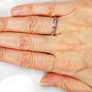 May include: A close-up of a hand wearing a thin gold band with small clear stones set in the metal.