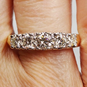 May include: A gold band ring with five round diamonds set in a row. The center diamond is larger than the other four diamonds.