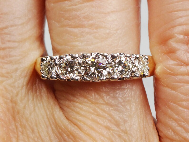 May include: A gold band ring with five round diamonds set in a row. The center diamond is larger than the other four diamonds.