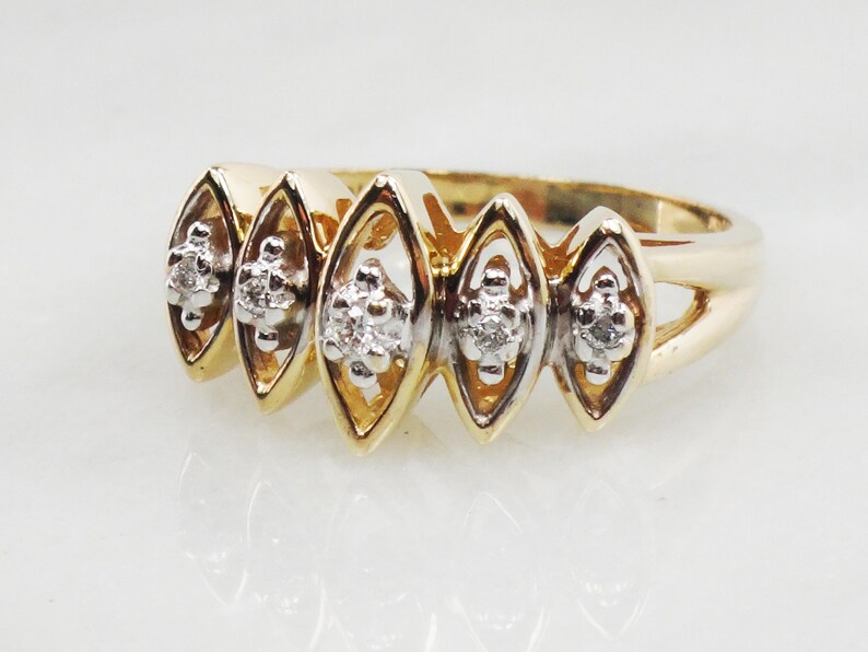 K&ouml;nnte beinhalten: Ein goldener Ring mit f&uuml;nf diamantf&ouml;rmigen Fassungen, jede mit einem kleinen Diamantencluster. Der Ring ist aus zweifarbigem Gold gefertigt, mit einem gelbgoldenen Band und wei&szlig;goldenen Fassungen.