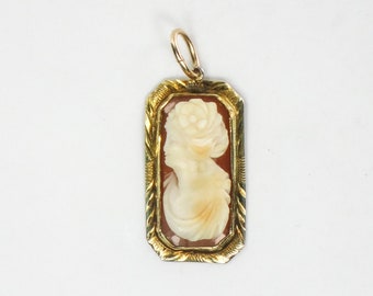 May include: A gold pendant with a cameo of a woman's profile in a white shell cameo. The cameo is set in a gold frame with a detailed design.