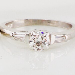 May include: A silver engagement ring with a single round diamond and two baguette diamonds on the band.