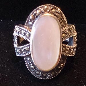 May include: A silver ring with a large oval-shaped pink stone set in a frame of black marcasite stones.