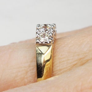 May include: A gold and white band ring with a row of small diamonds set in a prong setting.