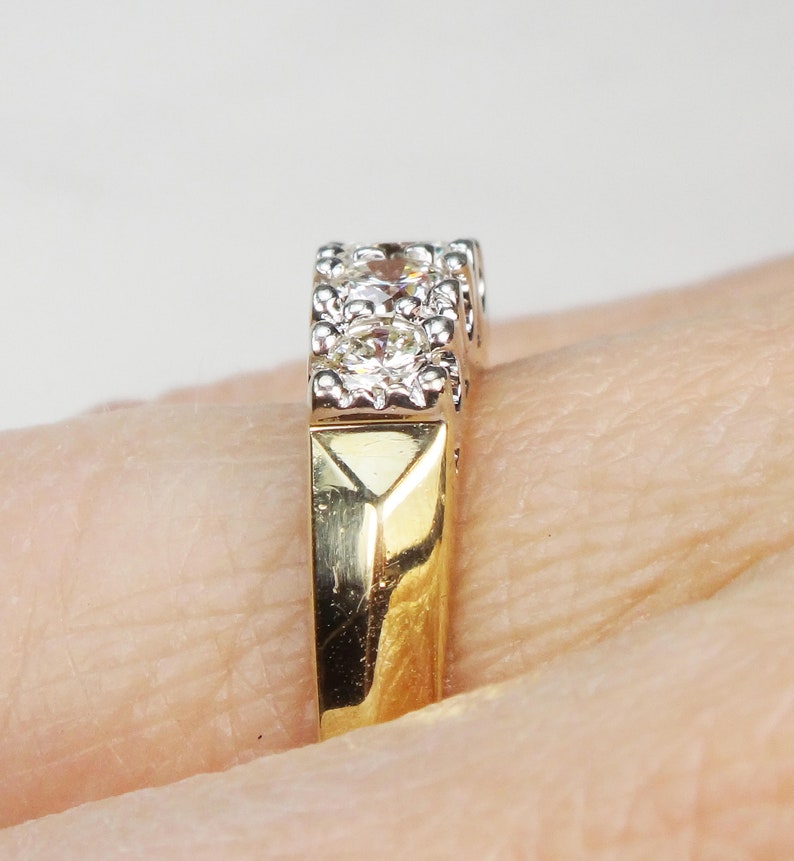 May include: A gold and white band ring with a row of small diamonds set in a prong setting.