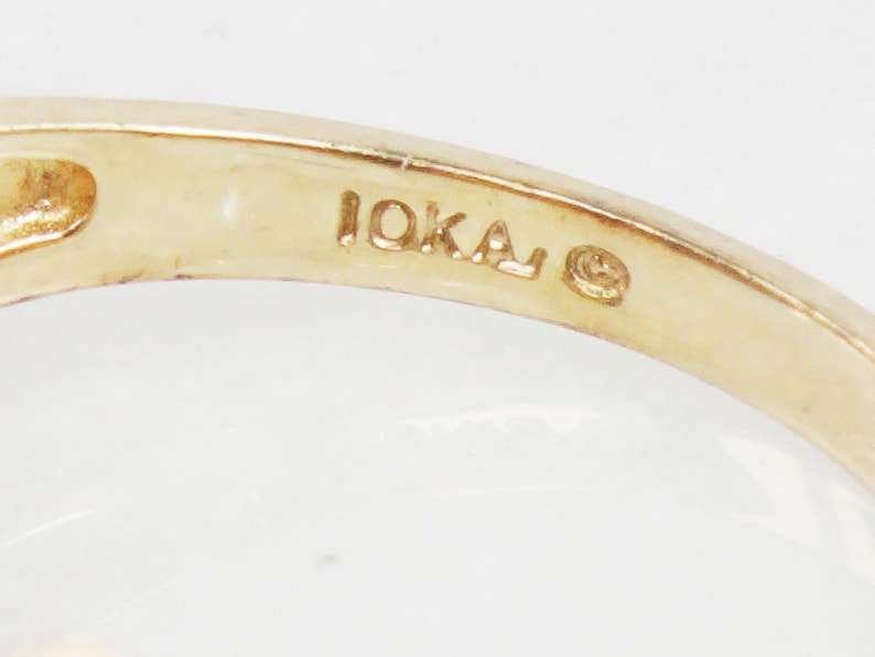 K&ouml;nnte beinhalten: Nahaufnahme der Innenseite eines Goldrings mit der Inschrift "10KA" und einem kleinen Kreis.