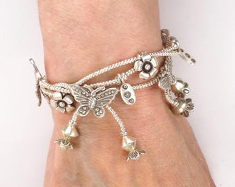 May include: A silver-toned multi-strand bracelet featuring metallic charms shaped like butterflies, five-petaled flowers, and small oval discs with circular indentations, all suspended from a delicate beaded chain design.
