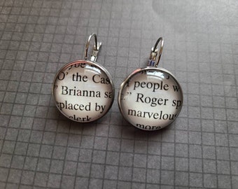 May include: A pair of silver dangle earrings with glass round charms. The charms feature text from a book, "O' the Cas" and "people w Roger sp marvelou more".