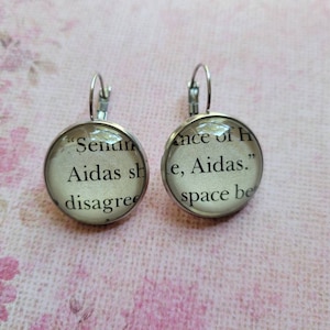 Puede incluir: Un par de pendientes de plata con abalorios de cristal. Los abalorios presentan texto de un libro, "Senin Aidas sh disagree" y "Ance of h le, Aidas." space be"