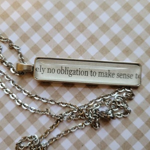 Puede incluir: Un collar de cadena de plata con un colgante rectangular que dice "No tengo absolutamente ninguna obligación de tener sentido para ti".