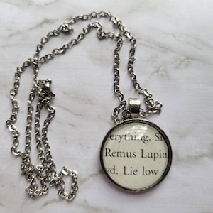 May include: A silver chain necklace with a round pendant featuring the text "everything.  Stay close. Remus Lupin.  Always.  Lie low."