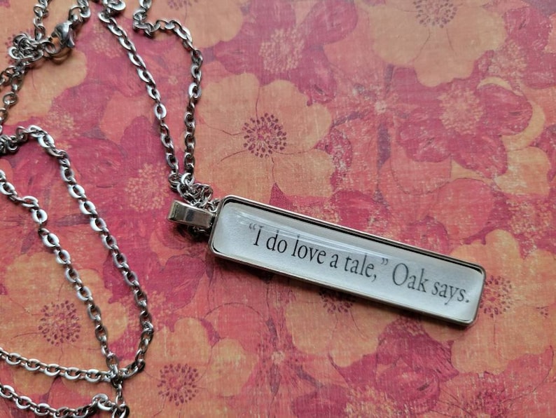 Op de afbeelding: Een zilveren ketting met een rechthoekige hanger met de tekst "Ik hou van verhalen, zegt Eik."
