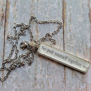 Puede incluir: Un collar de cadena plateada con un colgante rectangular de vidrio que dice "So pull yourself together, wo".