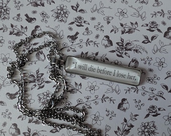 Könnte beinhalten: Silberfarbene Halskette mit rechteckigem Anhänger. Der Anhänger trägt den Schriftzug "I will die before I lose her," in schwarzer Schrift. Der Hintergrund ist ein Blumenmuster in Grau und Weiß.