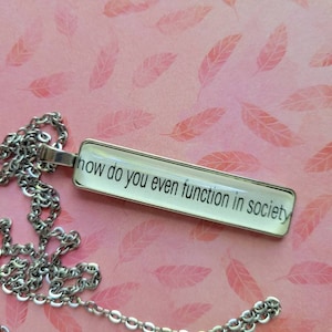 Puede incluir: Un collar de cadena plateada con un colgante rectangular de vidrio que dice "how do you even function in society".