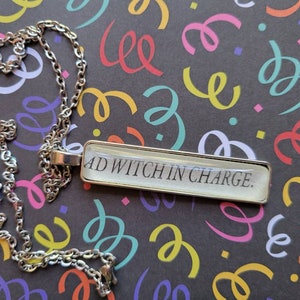 Puede incluir: Un collar de cadena plateada con un colgante rectangular que dice "#D Witch in Charge."