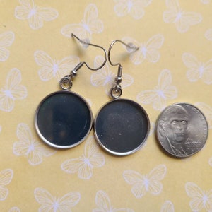 Op de afbeelding: Een paar zilveren oorbellen met ronde, zwarte, glasachtige cabochons. De oorbellen worden naast een Nederlandse 20-cent munt getoond ter vergelijking van de grootte.