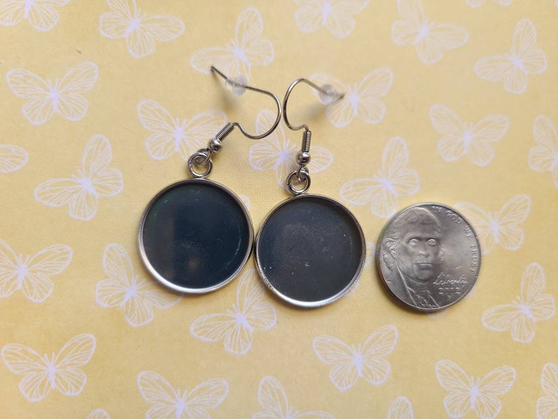 Op de afbeelding: Een paar zilveren oorbellen met ronde, zwarte, glasachtige cabochons. De oorbellen worden naast een Nederlandse 20-cent munt getoond ter vergelijking van de grootte.