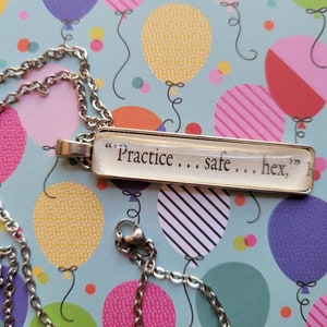 Puede incluir: Un collar de cadena plateada con un colgante rectangular de vidrio que dice "Practice... safe... hex," sobre un fondo colorido.