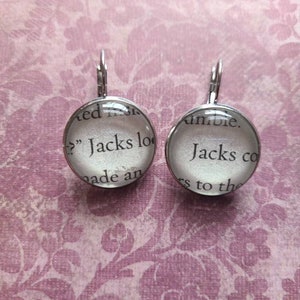 May include: A pair of silver earrings with glass round charms. The charms have a white background with black text that reads "Jacks loo" and "Jacks co".