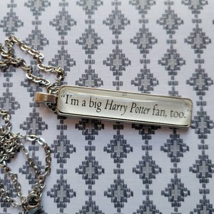 Peut inclure: Un collier en chaîne argentée avec un pendentif en verre transparent qui dit "Je suis un grand fan d'Harry Potter, aussi."