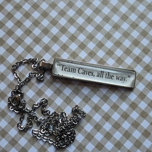 Puede incluir: Un collar de cadena de plata con un colgante rectangular de vidrio que dice "Team Caves, all the way."