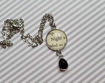 Könnte beinhalten: Eine silberne Kettenkette mit einem runden Anhänger mit dem Text "Night was ended us in" und einem schwarzen tropfenförmigen Anhänger.