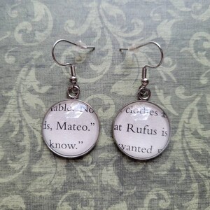 Pu&ograve; includere: Un paio di orecchini pendenti in argento con ciondoli rotondi in vetro. I ciondoli presentano testo da un libro, "able. No ds, Mateo." e "clothes a at Rufus is wanted".