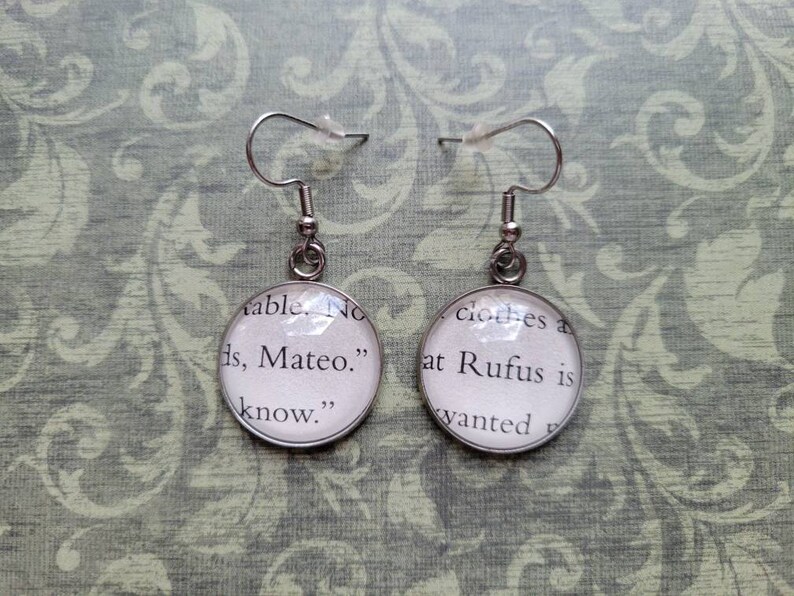 Pu&ograve; includere: Un paio di orecchini pendenti in argento con ciondoli rotondi in vetro. I ciondoli presentano testo da un libro, "able. No ds, Mateo." e "clothes a at Rufus is wanted".