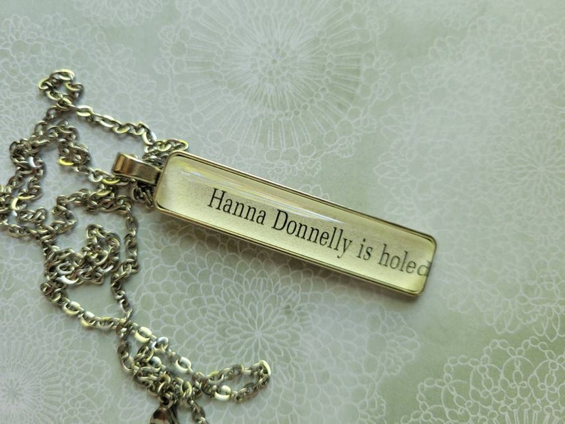 Puede incluir: Un collar de cadena plateada con un colgante de vidrio transparente que dice "Hanna Donnelly is holed".