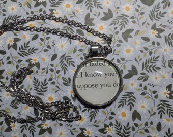 Könnte beinhalten: Eine silberfarbene Halskette mit einem runden Anhänger mit Text. Der Anhänger hängt an einer Kette mit einem Karabinerverschluss. Der Hintergrund ist ein Blumenmuster mit weißen Gänseblümchen und grünen Blättern auf hellblauem Grund.