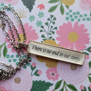 Puede incluir: Un collar de cadena de plata con un colgante rectangular de vidrio que dice "There is no end to our story."