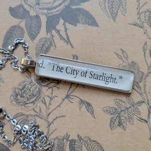 May include: A silver chain necklace with a rectangular pendant that reads "The City of Starlight."