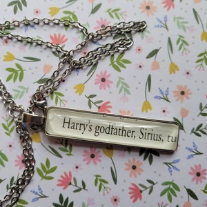 May include: A silver chain necklace with a rectangular pendant that reads "Harry's godfather, Sirius, tu"