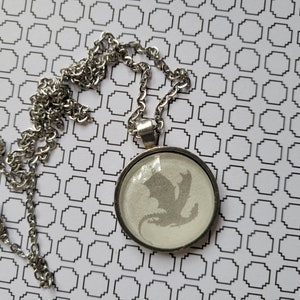 May include: A silver chain necklace with a round pendant featuring a white silhouette of a dragon.