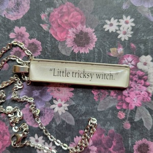 Op de afbeelding: Een zilveren ketting met een rechthoekige hanger met de tekst "Little tricksy witch."