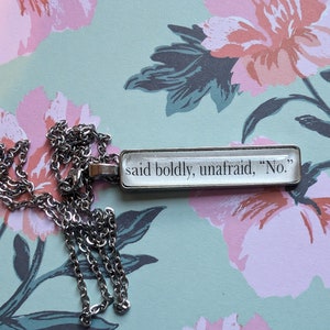 Puede incluir: Un collar de cadena de plata con un colgante rectangular que dice "said boldly, unafraid, "No.""